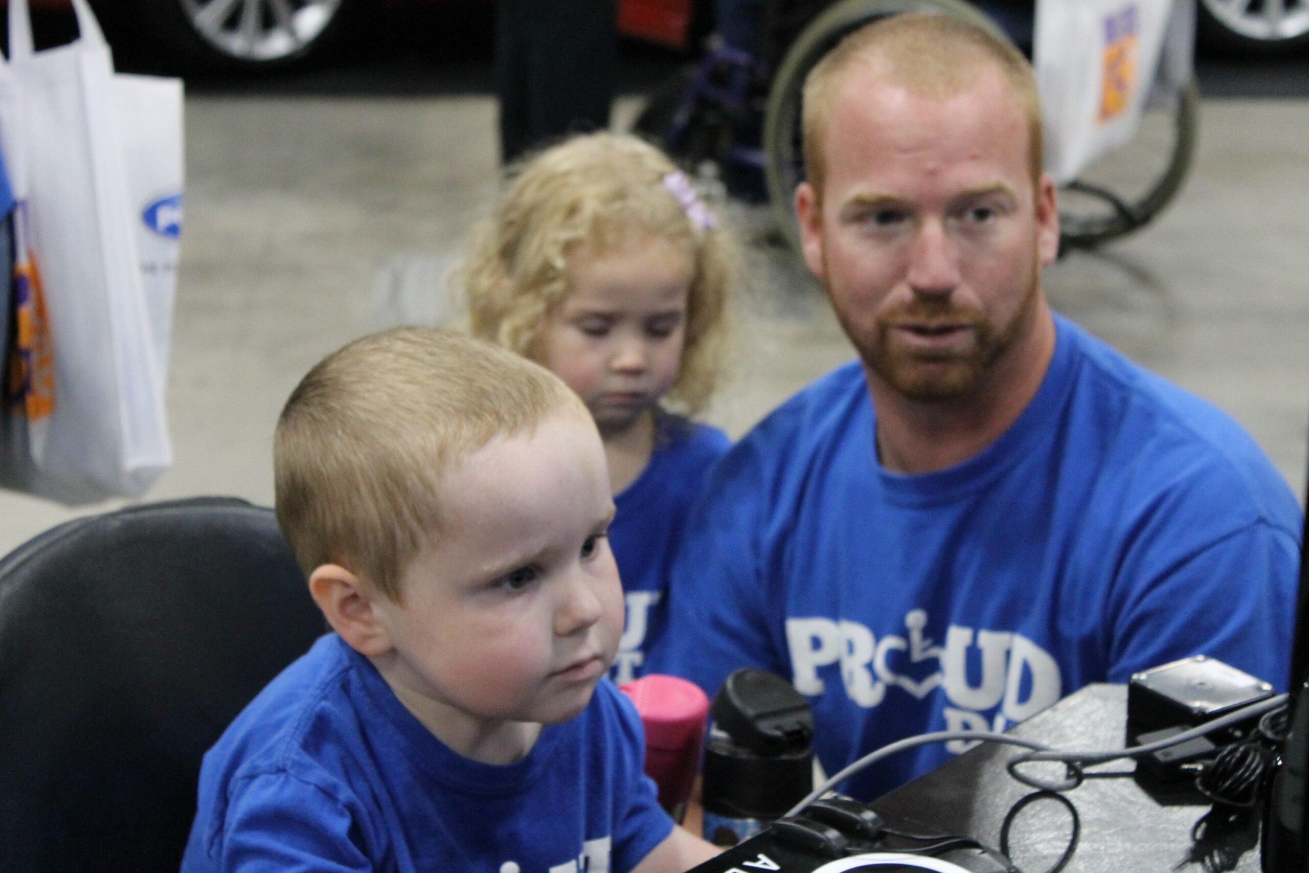 A young boy in a wheelchair and his father and sister play a videogame