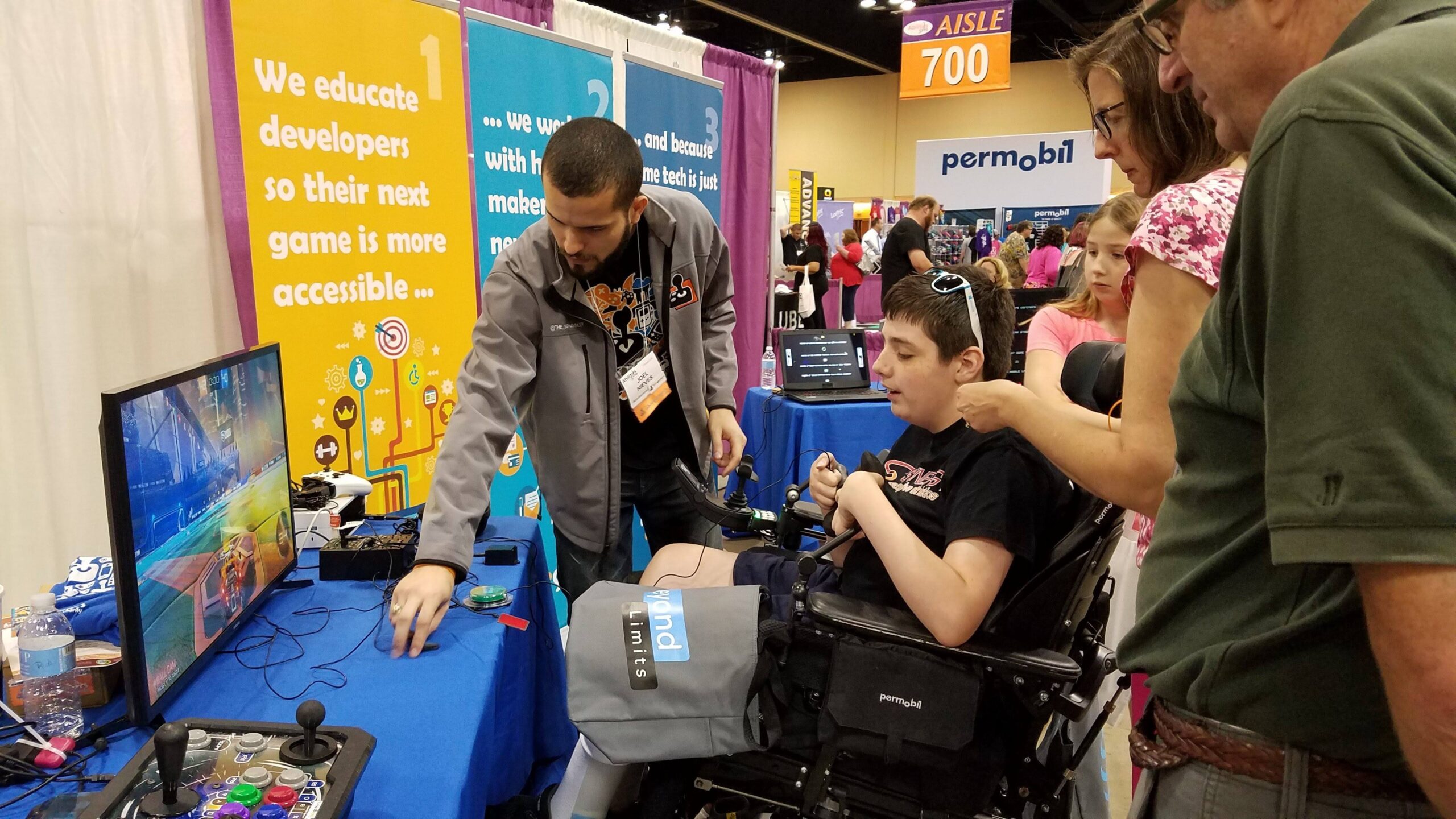 At an expo, man demonstrates videogame to teen in wheelchair and companions